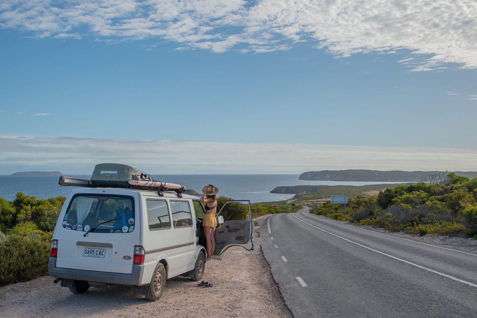 A woman stands next to a white van on a sunny day, looking at the coastline in the Dhilba Guuranda-Innes National Park in South Australia's Eyre Peninsula. 