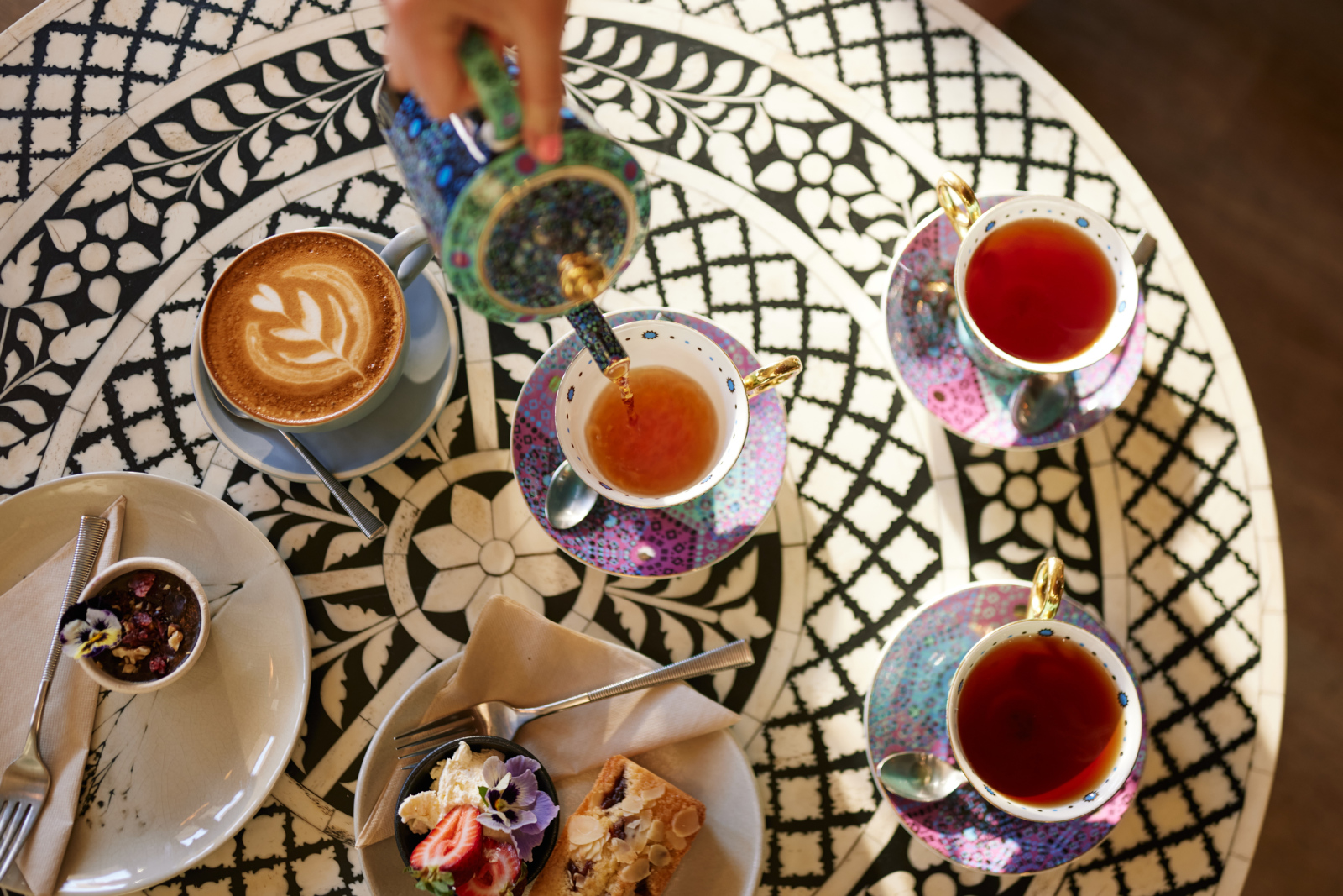 A colourful table with coffee, cake and cups of tea being poured. 