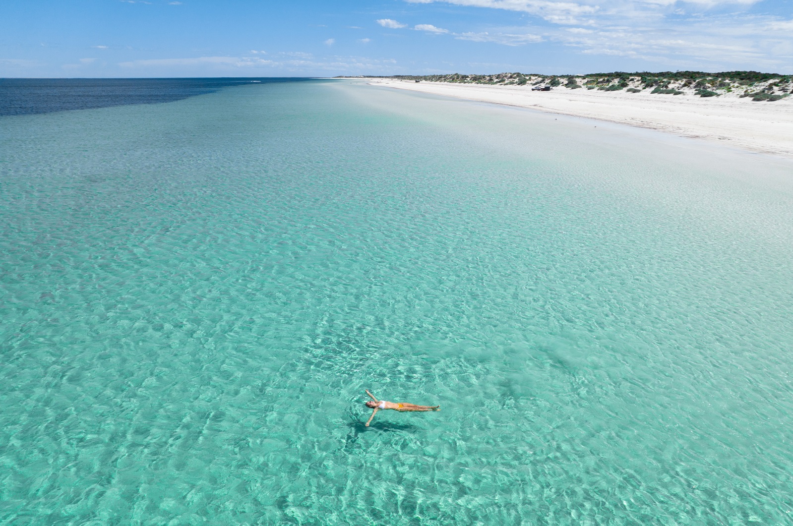 A woman floating in crystal blue waters on a sunny day at Wauraltee Beach, Yorke Peninsula
